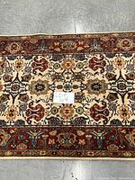 Close-up view of cream field area rug with rust red border and floral pattern, showing detail of pattern and colors.