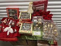Photo showing assorted Christmas tree decorations including boxes of glass baubles in various colors and designs, red poinsettia flowers, angel tree topper, small fabric ornaments, red tree skirt, and a tree storage bag.