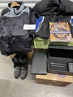 Overall view of men's motorcycle rain jacket, textile touring jacket, boots, books, and BMW log book box arranged together.