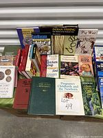 Photo of a mix of hardcover and paperback books arranged with visible titles including Indian Fishing, Pig War, Chicken Soup for the Woman's Soul, and more.