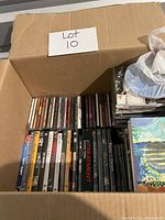 Box containing various CDs, DVDs, and Blu-Rays, with spines of cases visible showing a range of titles and genres