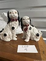 Front view of two black and white ceramic dog figurines on a wooden surface, both with red bow ties.