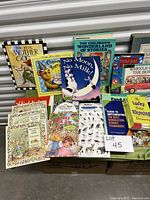 Photo showing a collection of children's books and educational aids arranged on a table including titles such as The Real Mother Goose, No Moon, No Milk, Wheels on the Bus, and teaching aids.