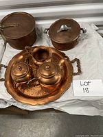 Copper lot with two pots with lids, copper serving tray, tea pot, creamer, and sugar bowl arranged on white paper.