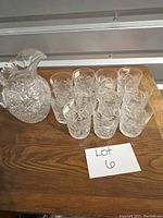 Full set of one crystal pitcher and ten glasses arranged on wooden surface for scale and count.