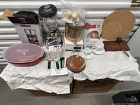 Kitchen lot displayed including blender, food processor, cappuccino set, microwave dish, cheese board, and wine cork screws.