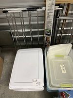 Photo showing metal laundry drying rack, white plastic storage totes with lids stacked, and part of wooden drying racks and furniture in background.