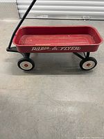 Side view of red Radio Flyer wagon showing metal body, wheels, and black pull handle.