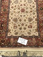 Close-up of the rug showing floral design and fringe at the end with lot number reference.