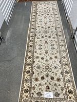 Full view of cream-colored floral runner rug laid on floor, showing decorative border and middle design.