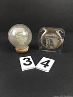 Front view of two vintage Niagara souvenir paperweights: clear glass spherical and square shapes with embedded images and metallic accents.