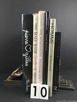 Front view of six male nude photography books standing upright between two bookends, spines visible.