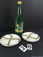 Two decorative plates with abstract black and yellow lines, photographed with a Perrier lemon-lime bottle for scale.