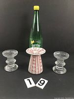 Front view of two clear glass candle holders flanking a red-patterned ceramic candle holder placed in front of a Perrier bottle, illustrating size and condition.