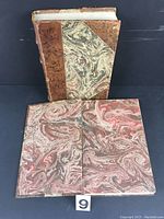 One vintage book standing and a second book laying flat with marbled covers visible.