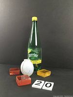 Photo of all items including the small white decorative vase and three colored glass cubes, an orange-red pair and one amber-yellow, with a Perrier lemon soda bottle for size reference.