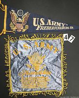 Photo showing U.S. Army felt pennant banner with embroidered eagle and text, alongside gray satin fringe banner with gold text and emblem.