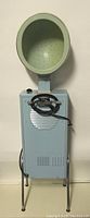 Front view of vintage Simpsons Sears hairdryer, showing green dome hood, blue body, cable, and metal legs.