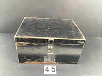 Closed vintage black metal box showing rubbed paint and scratches on edges and surface.