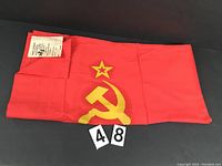 Folded red Soviet flag showing visible hammer and sickle emblem with star and label tag in corner.