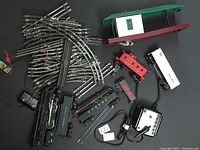 Overview of train tracks, red and green depot, controllers, locomotive and freight cars laid out on black surface