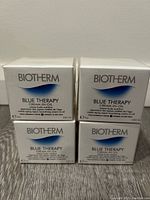 Four sealed Biotherm Blue Therapy Cream-in-Oil boxes stacked in 2x2 formation, front view showing product name and volume.