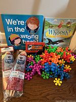 Lot overview showing 2 books, 2 dolls, red toy truck, and pile of colorful building set pieces on table.