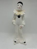 Front view of porcelain clown figurine, showing white suit, ruffled collar, black cap, face, and pink rose in hand.