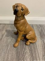 Front view of brown Labrador dog figurine sitting on floor with detailed fur texture and expressive eyes.