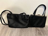 Two black evening purses side by side; Guess brand rectangular bag with longer handles on left, Gap brand square structured purse with shorter handles on right