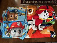 Full view of folded bedding set including fitted sheet, flat sheet, pillowcase, duvet, and blanket with Marshall stuffed animal on top.