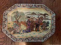 Full view of the octagonal vintage Satsuma plate depicting Geisha figures near a bridge and willow trees with a mountain background, showing overall size and intricate border details.