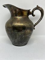 Front and side view of the silver plated water pitcher showing tarnishing on the surface and details on the spout and body shape.