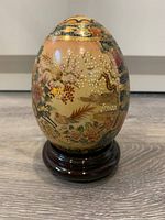Full view of the ceramic egg showing floral and bird details with gold Moriage accents on a wooden base