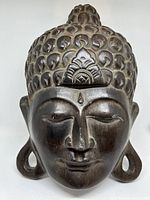 Front view of the dark wooden carved Buddha head showing face, hair detail, and elongated ears.