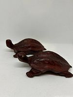 Two small reddish-brown wooden turtle carvings viewed side by side on a flat surface, showing profile and top shell details.