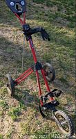 Full view of the red 3-wheeled Bag Boy golf caddy standing on grass, showing the frame and wheels