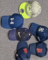 Photo of six new baseball caps on carpeted floor: 2 Milwaukee Brewers, 2 New York Yankees, 1 Under Armour and 1 Nike.