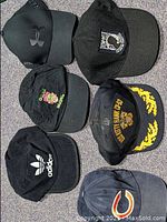 Six baseball caps arranged in two columns of three caps on floor showing front logos and colors clearly.