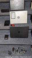 Photo showing three laptops (Gateway, silver HP, black HP) along with black rectangular Bluetooth speaker, Dell Intel tablet, Seagate portable hard drive, red computer mouse, and assorted computer cables and chargers, plus two flashlights.