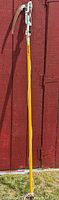 Full view of the Wallace tree branch saw leaning against a red wooden surface showing the long yellow handle and attached saw blade at the top.