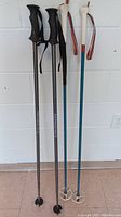 Full view of two pairs of ski poles: one black pair with Salomon branding and black grips, one teal pair with white grips and striped wrist straps.
