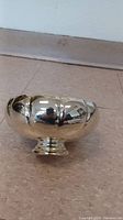 Silver footed bowl sitting on floor showing rounded lobed sides and reflective surface.