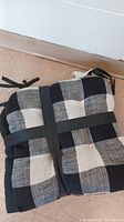 Folded black and white checkered seat cushions showing tuck buttons and black borders held together by a strap