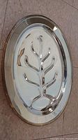 Oval silver-tone tray with central embossed tree branch and star details, decorative edging visible