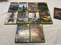 Top-down image showing all 12 Xbox game cases arranged in a grid on a flat surface. Titles and cover art clearly visible.