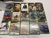 Photo showing all 15 Xbox games laid out on white fabric background, includes cases and disc for Halo 2.