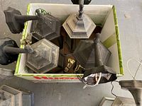 Photo of 7 outdoor light fixtures inside a cardboard box, showing dust and dirt accumulation on metal frames and glass panels.