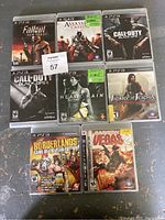 Photo showing front covers of 8 PlayStation 3 game cases arranged in three rows on a surface. Titles visible are Fallout New Vegas, Assassin's Creed II, Call of Duty Black Ops, Call of Duty Black Ops II, Heavy Rain, Prince of Persia The Forgotten Sands, Borderlands Game of the Year Edition, and Rainbow Six Vegas 2.