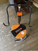 Front view of Ab Doer Twister machine showing black and orange padded seat, handle bars, and frame